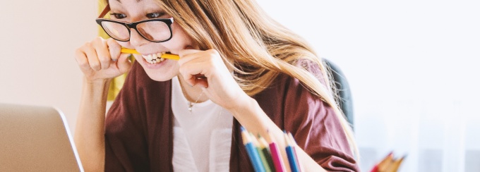 photo of a girl biting a pencil while looking at a laptop.