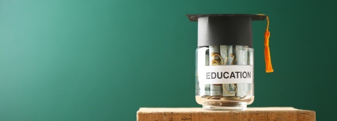 A jar sitting on books with money in it. The jar is labeled "education" with a graduation cap on it. 