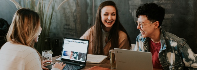 photo of four people looking at a laptop screen in a library or coffee shop.