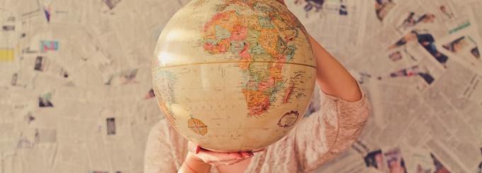 Photo of a person holding a globe in front of their face. 