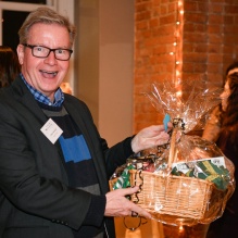 man holds up basket containing goods he'd won at an auction. 