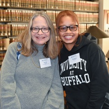 professor and student standing in a library, smiling as they pose together. 