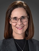 Woman wearing gold necklace, glasses, smiling. 