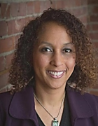 woman standing in front of a brick wall, smiling, wearing purple top and necklace. 
