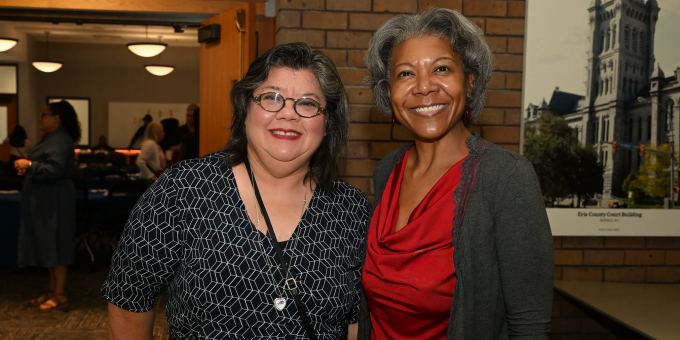 Two attendees pose for a photo at a law school networking event, standing in front of a brick wall near the entrance to a gathering space. 