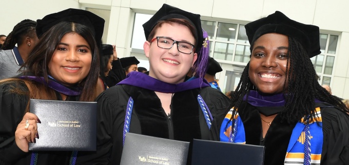 three recently graduated students wearing their commencement cap and gown. 
