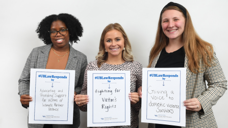 Three individuals standing side by side, each holding a sign with messages supporting victims of domestic violence as part of the #UBLawResponds initiative. 