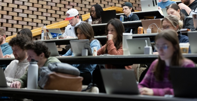 A classroom of students, some with laptops, listening to a classroom lecture. 