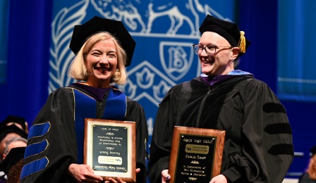 woman wearing graduation regalia, standing with an award.