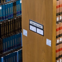 Rows of legal reference books and law reports on library shelves, with a shelf marker labeled “New York Court.”.