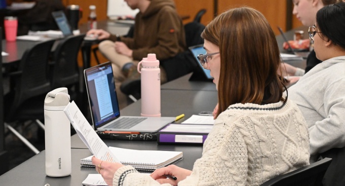 Students review course materials and work on laptops during an undergraduate law class. 