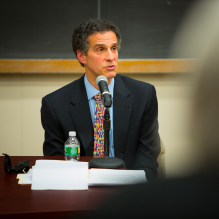 man sitting at a table speaking into a microphone. 