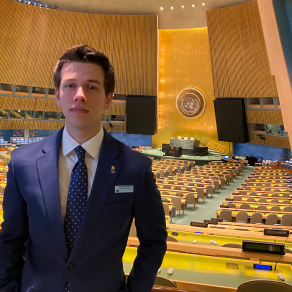 young man standing inside a large UN assembly room. 
