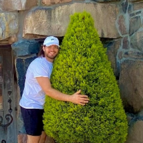 man outside hugging a bush. 