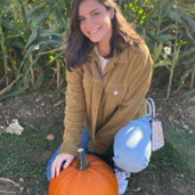 Kyli outside in a cornfield holding a pumpkin. 