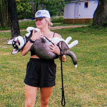 Young woman wearing baseball cap, outside, holding a husky puppy. 