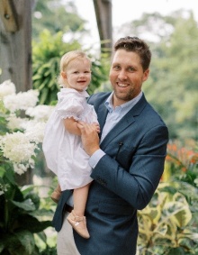 man holding baby outside in a garden. 