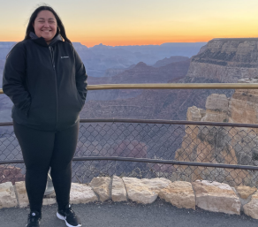 woman standing outside at the Grand Canyon as the sun sets. 
