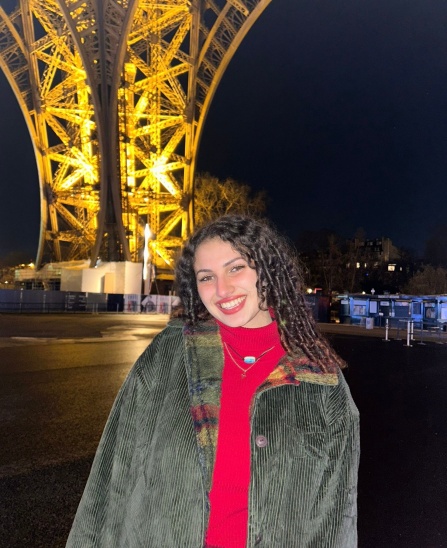Young woman standing in front of the Eiffel Tower at night. 