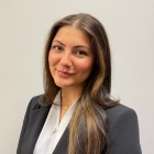 Woman smiling, wearing a black jacket and top, two gold necklaces. 