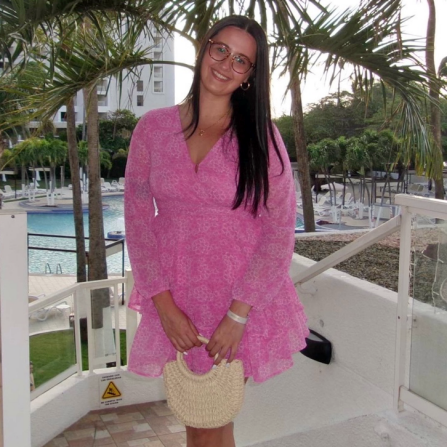 Young woman wearing pink dress, standing outside in a resourt. 