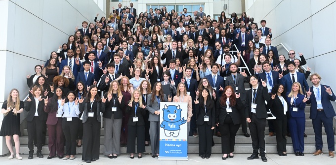 University at Buffalo School of Law students pose for a class photo outside a campus building, many making the UB horns hand sign. 