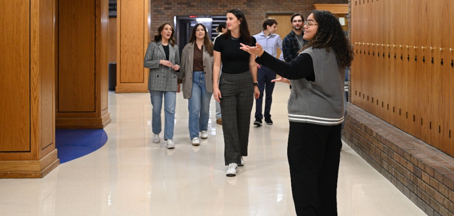 A young woman directing a group of students in a hallway of the law school building. 