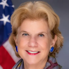 woman wearing blue earrings in front of a US flag. 