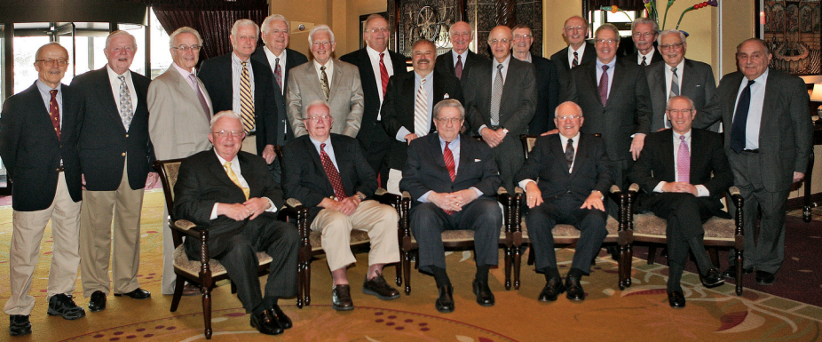 a group of men sitting inside a big room posing for a photo. 