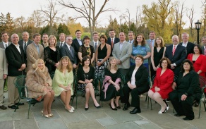 large group of people posing together for a photo, standing outside, some sitting in chairs. 