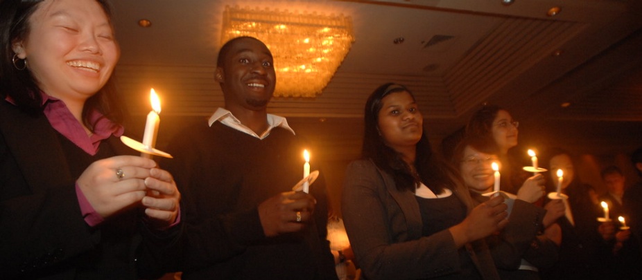 students standing with lit candles in a dim room. 