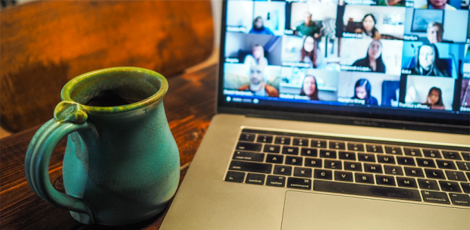 coffee mug sitting next to a computer, screen showing a zoom conference taking place. 