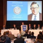 William Savino '75 stands at a podium, speakingn to a large group of people in a room. behind him is a screen that says 2023 Edwin F. Jaeckle Award with his photo. 
