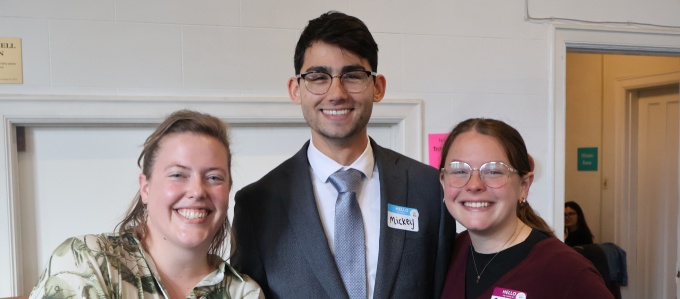 Three people standing together indoors, wearing name tags and posing for a group photo. 