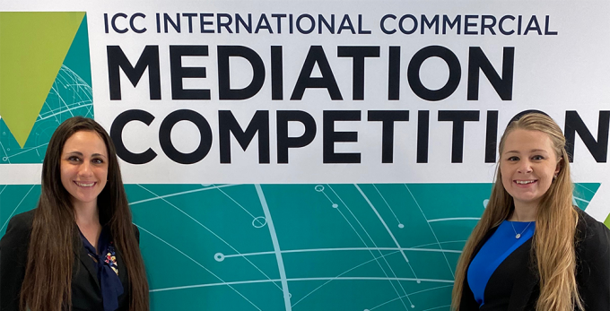 two law students standing in front of a mediation competition sign. 