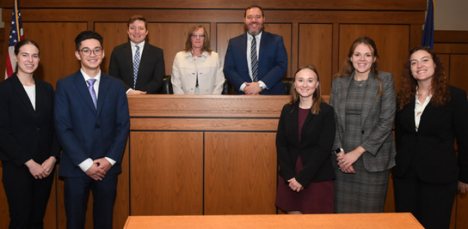 Group of people in a courtroom, wearing suits, smiling for a photo. 
