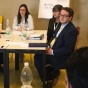 group of people sitting around a table, looking towards other people talking. 