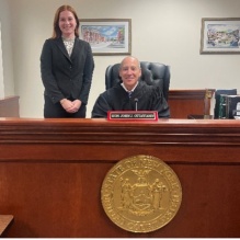 Young woman standing next to a male judge sitting at his bench in a courtroom. 
