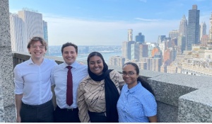 Group of young adults standing outside atop of a building with city skyline behind them. 