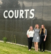 Three young women standing outside next to a wall with the word Courts.