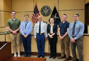 group of young professionals standing in a courtroom with flags behind them. 