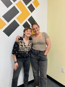 Two young women standing next to a graphic loco, smiling. 