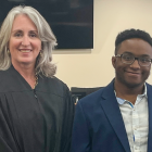 A judge in a black robe standing beside a person in a suit inside a courtroom. 