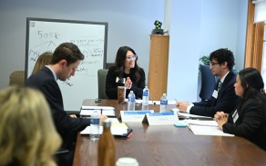 Law students participate in a team based advocacy exercise around a conference table while a facilitator leads the discussion.