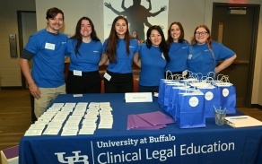 Volunteers staff a registration table at a University at Buffalo Clinical Legal Education event, with name tags, welcome materials, and gift bags displayed.