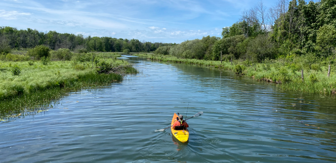 a person in a kaiyak, paddling down a blue channel on a sunny day. 