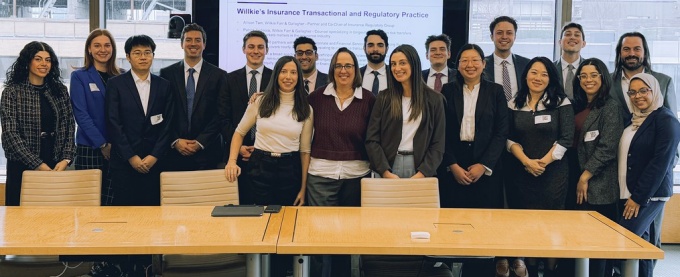 large group of people standing around a long table, smiling for their group photo. 