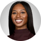 Professional headshot of a person with long straight hair, smiling, wearing a dark top against a light gray background. 