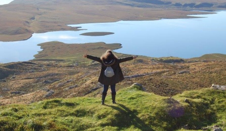 Zoom image: UB Law student standing with her back toward the camera facing a lake and mountains in Glasgow, Scotland.