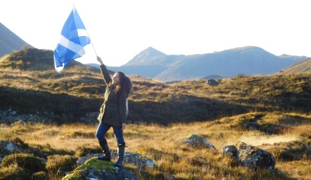 UB Law student standing on a rock holding a flag with mountains in the background in Scotland. 